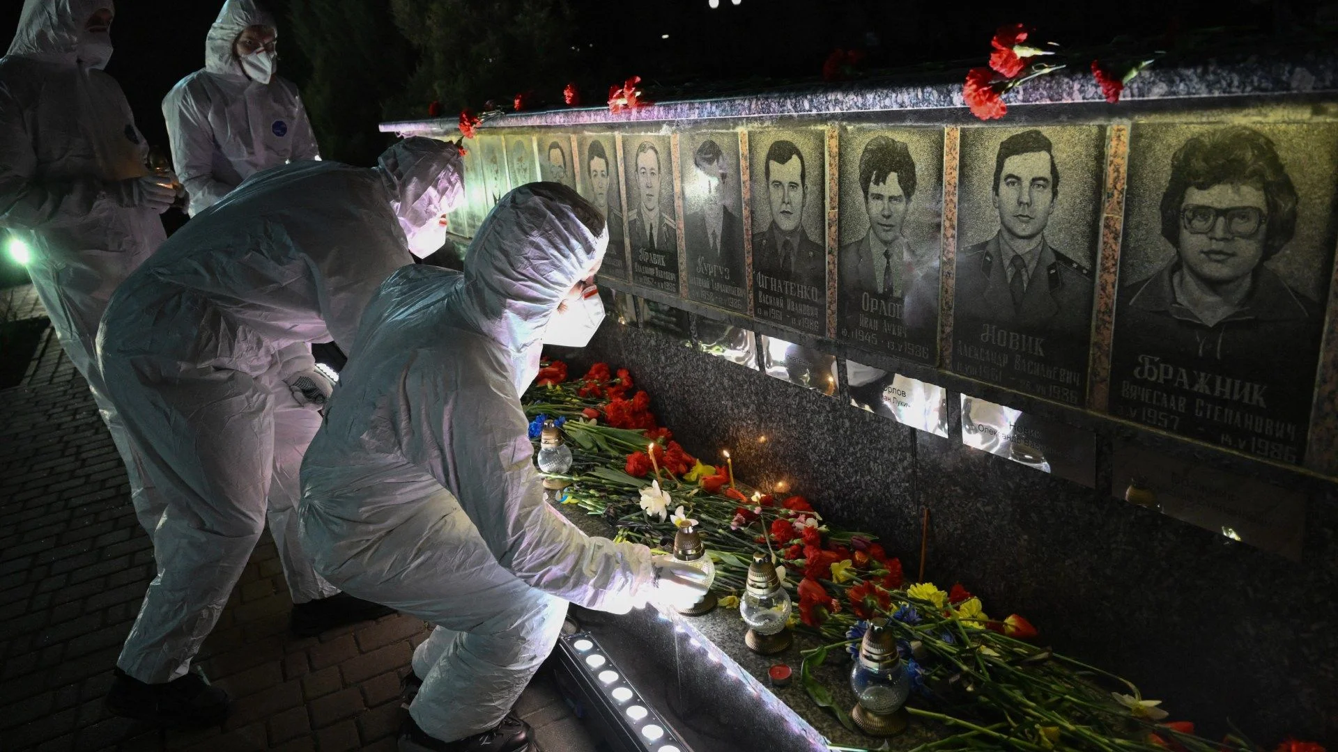 Participantes vestidos con trajes blancos de protección (hazmat), representando a los liquidadores, colocan velas frente a un monumento en memoria de las víctimas de Chernóbil, durante una ceremonia conmemorativa por el 40 aniversario de la explosión en la central nuclear de Chernóbil, el peor desastre nuclear civil de la historia, en la ciudad de Slavutych.